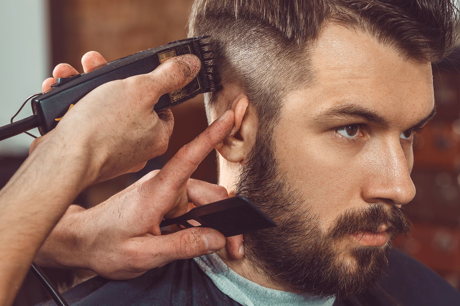 Barber trimming a man’s beard and hair with clippers in a salon