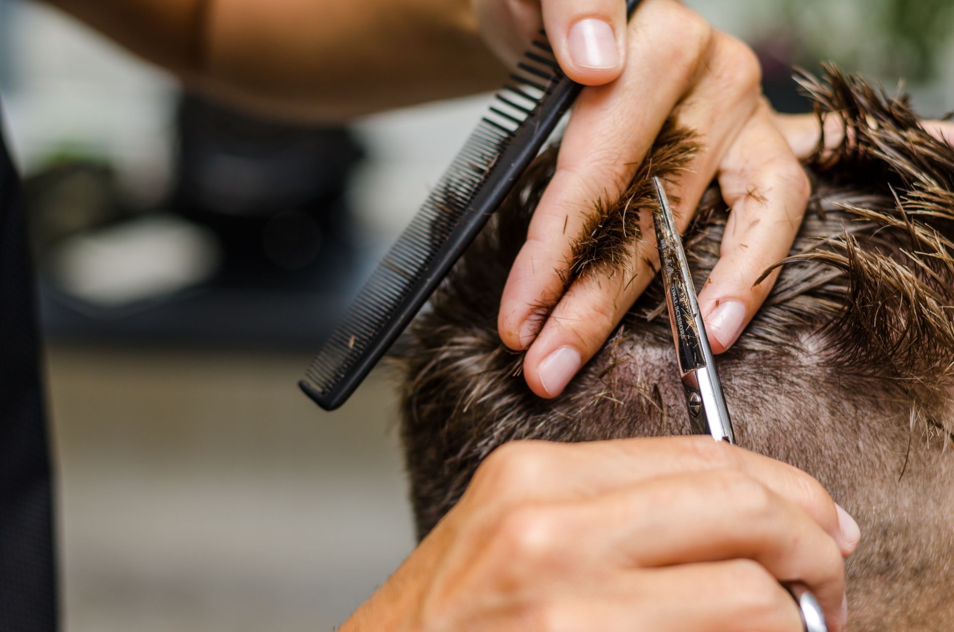 Hairdresser combing and trimming a client’s short hair with scissors in a salon