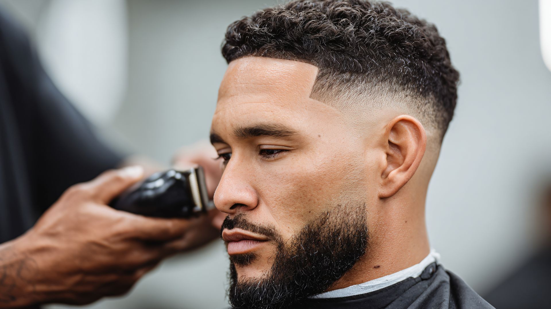 Barber trimming a man’s beard with electric clippers in a salon