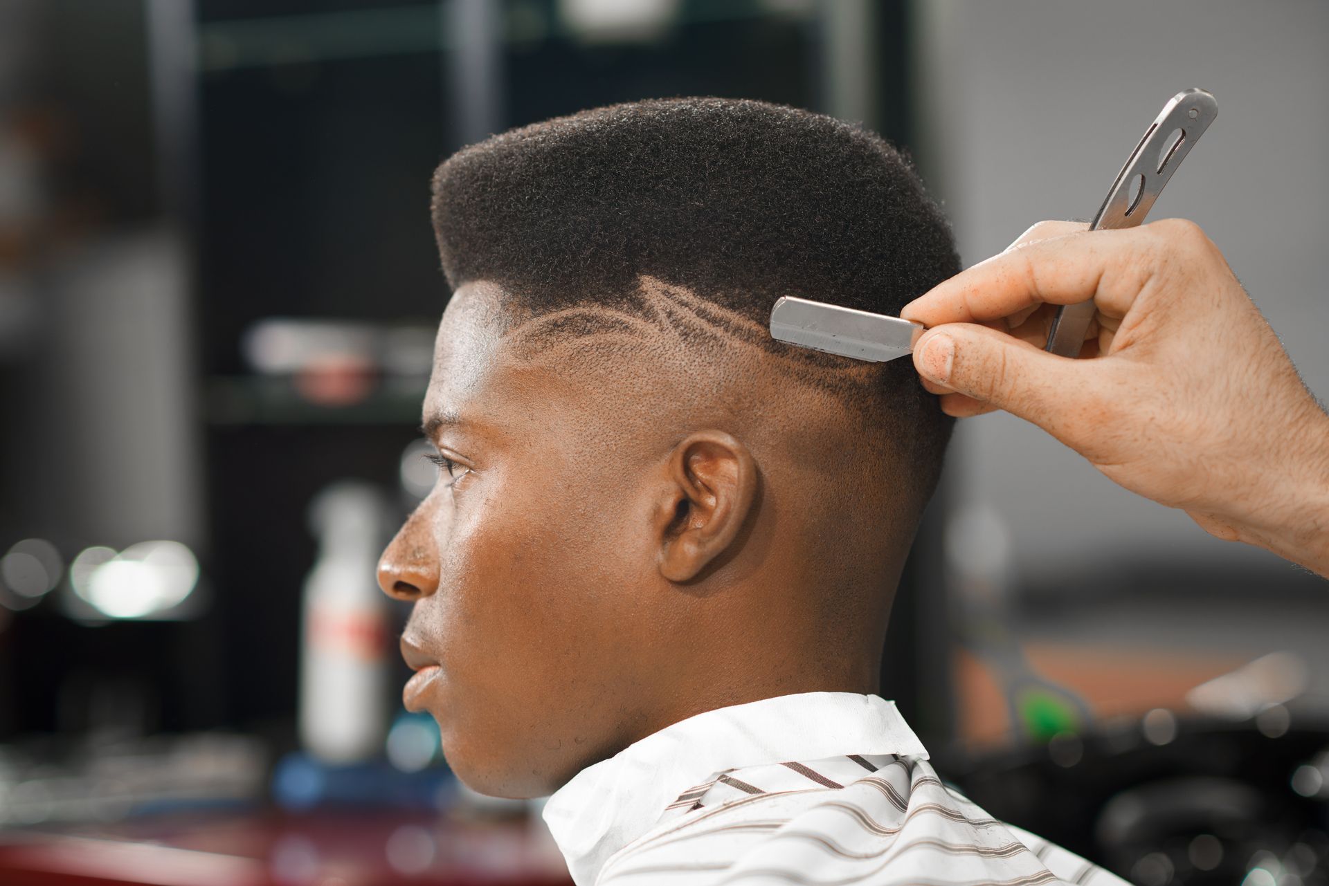Barber shaving a design into the side of a person's high-top haircut with a straight razor.