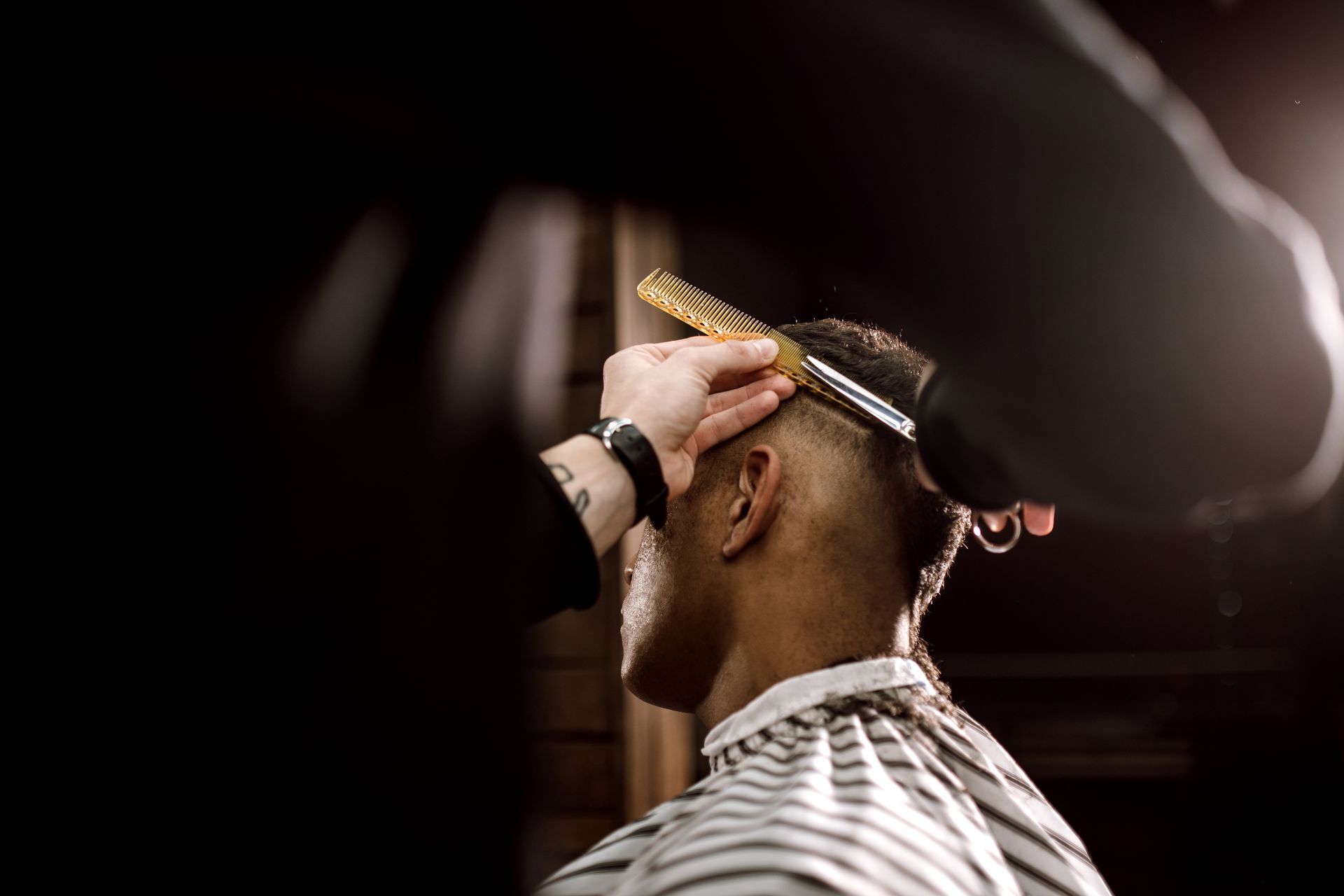 Barber trimming a client's fade with electric clippers under bright salon lights