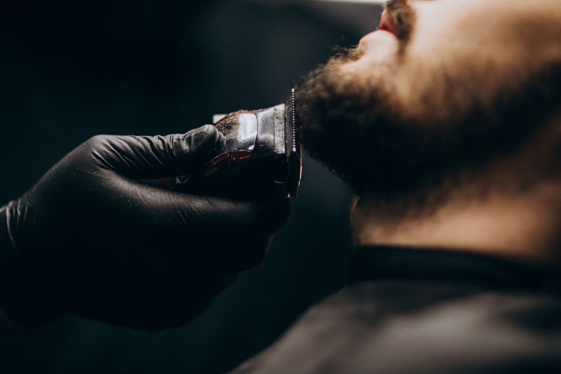 Barber trimming a bearded man's neck with electric clippers