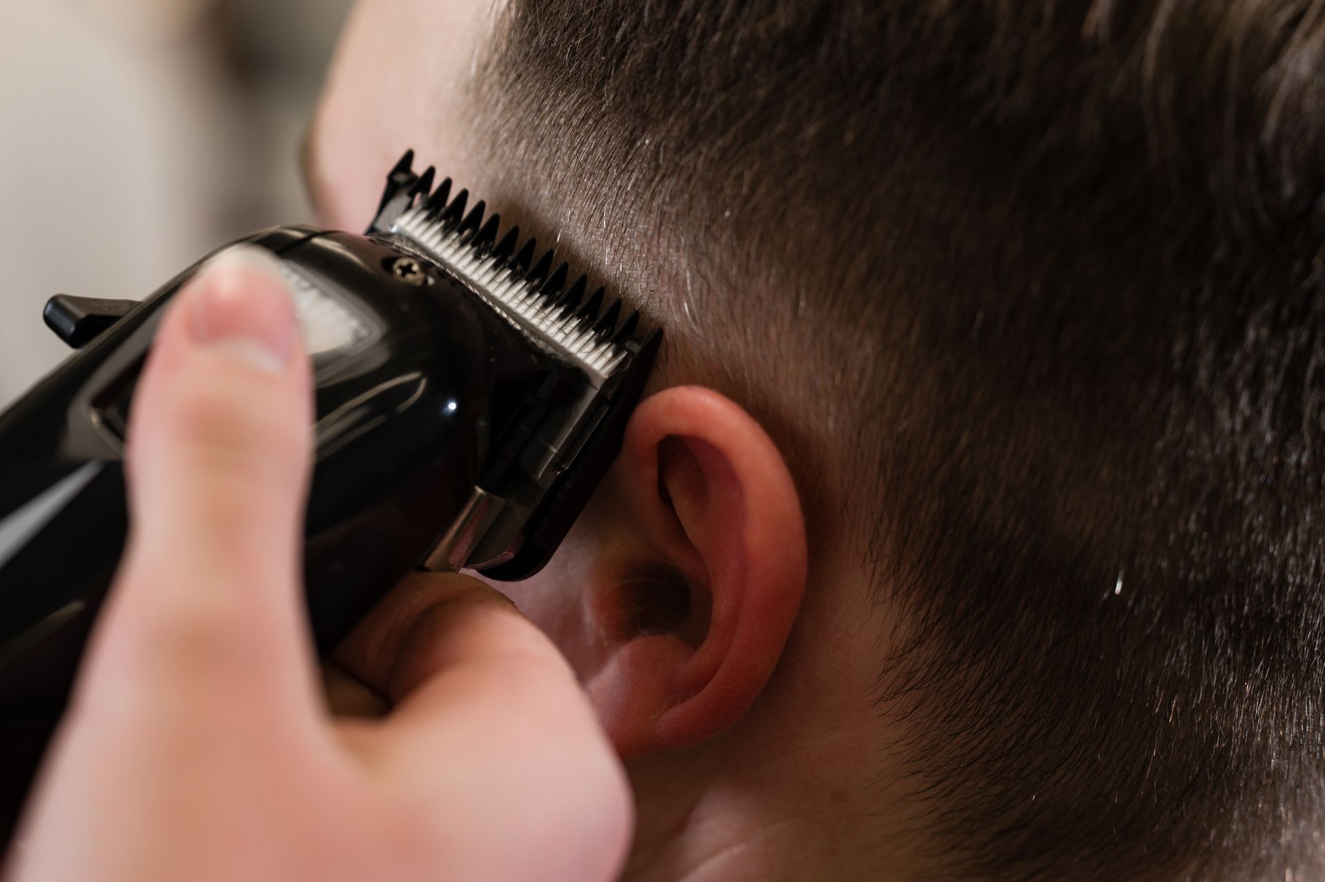 Hair clippers trimming the side of a person’s head near the ear