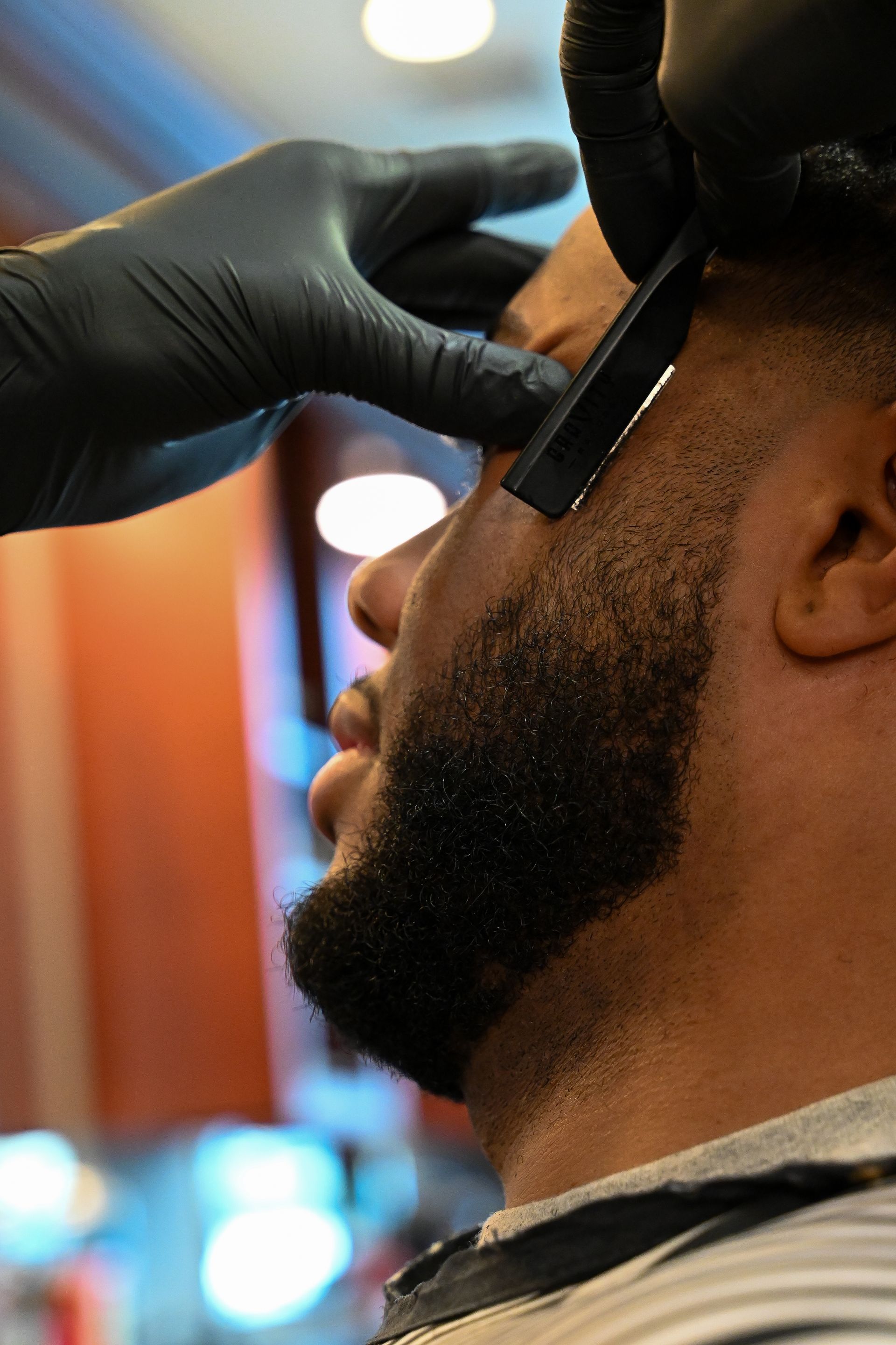 A man is getting his beard shaved by a barber wearing black gloves.