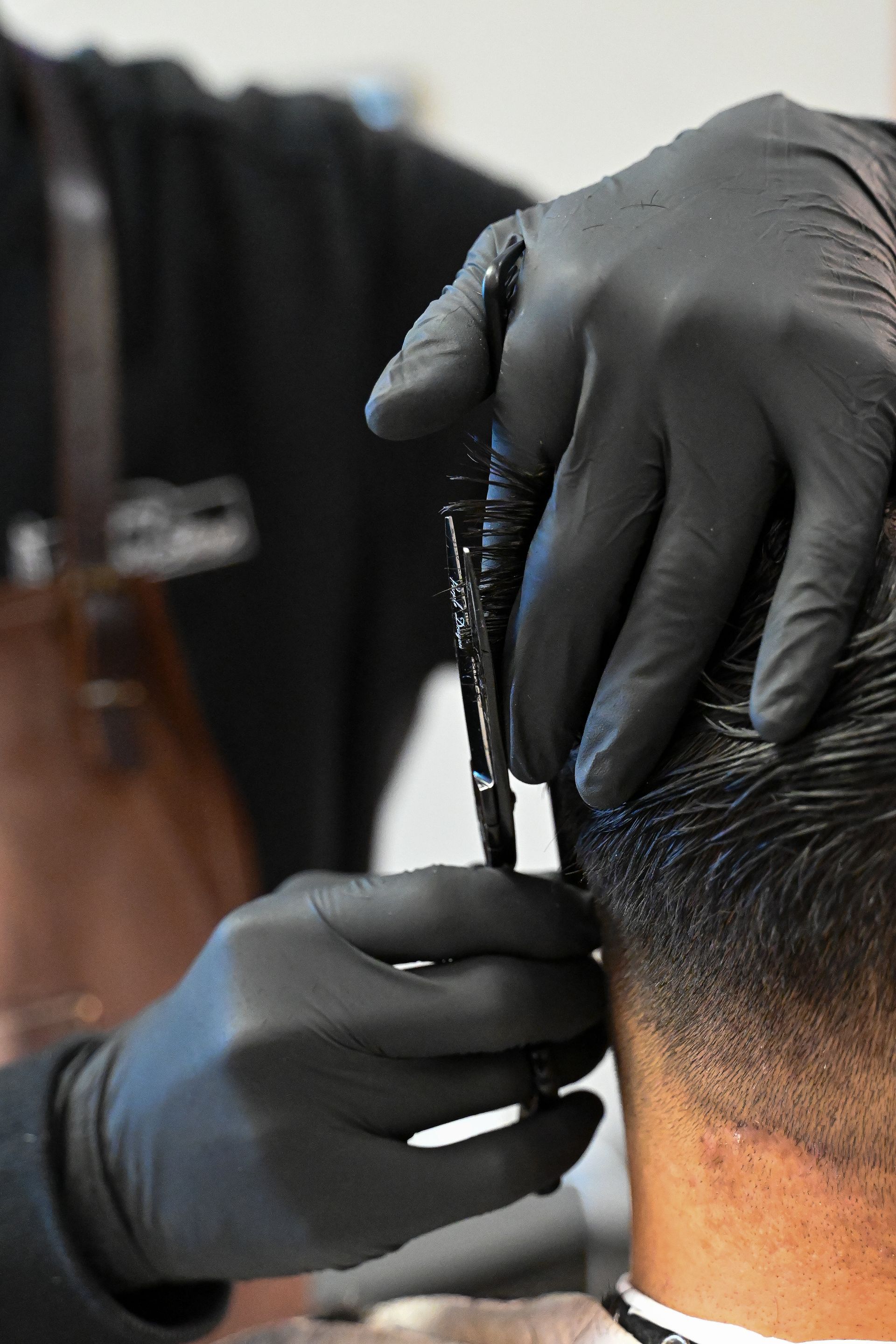 A man is getting his hair cut by a barber wearing black gloves.
