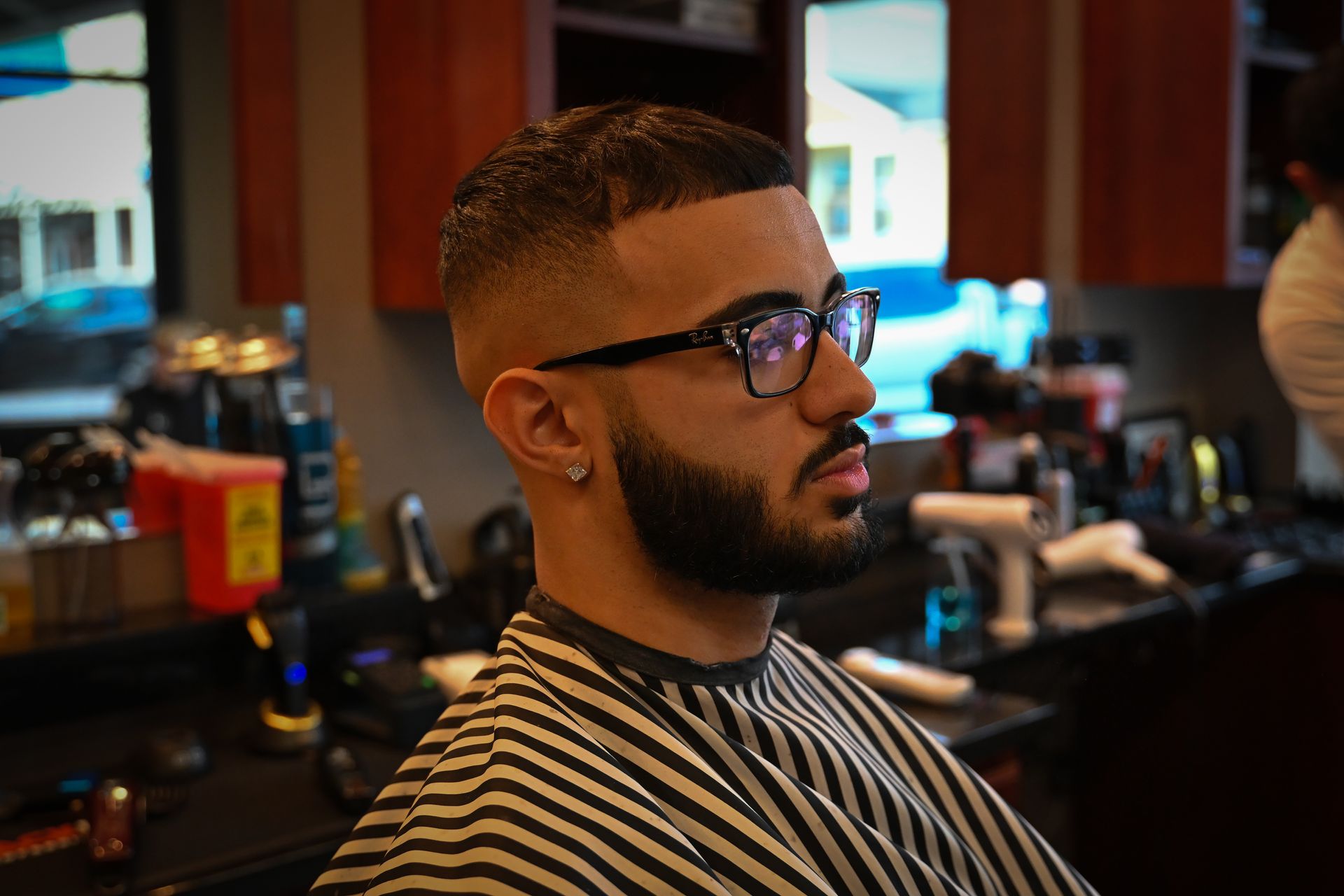 A man with a beard and glasses is getting his hair cut at a barber shop.