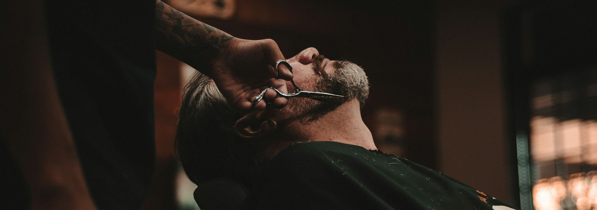 Barber trimming a man’s beard with clippers in a dimly lit salon