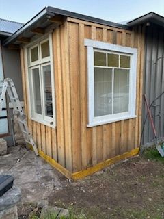 Small wooden structure with two white-framed windows, built onto a larger building, outdoors.