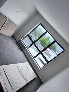 Room with large window, gray carpet, white walls, cardboard boxes.