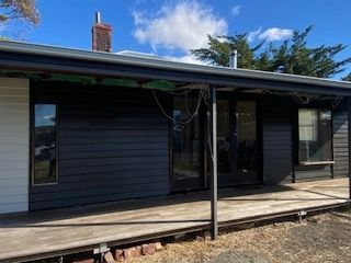 Black-sided house with a porch and wooden deck, against a blue sky with trees in the background.