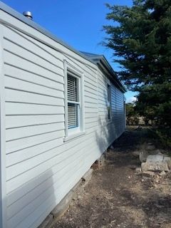 White-sided building with window and closed blinds, dark ground, and blue sky.