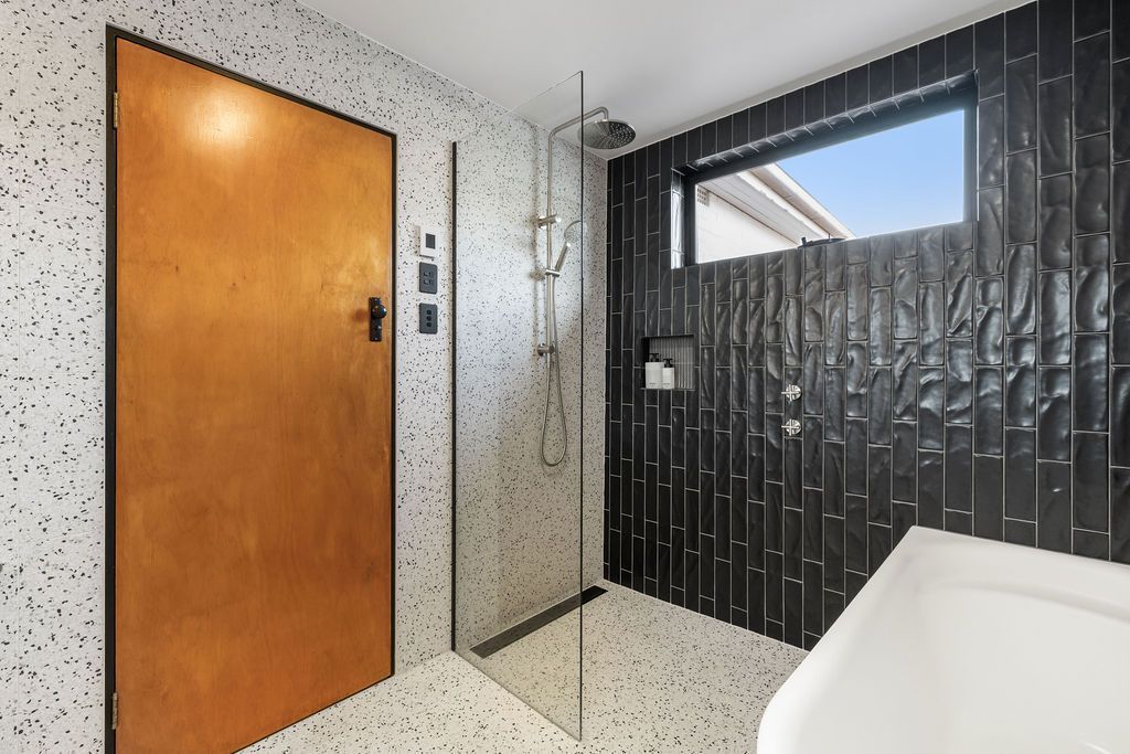 Small tiled room with wooden door, speckled walls, and a frosted window covered by black blinds.