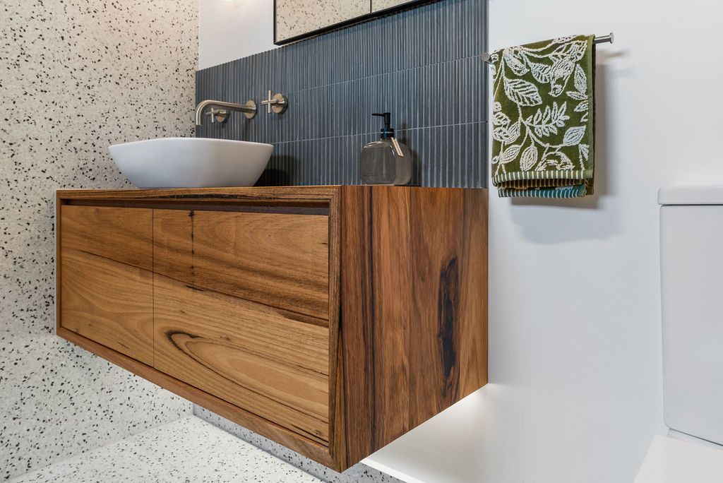 Wood vanity with vessel sink and faucet in a modern bathroom, with patterned towel and speckled walls