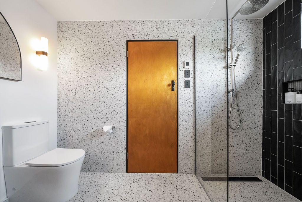 Modern bathroom with speckled tile, wood door, toilet, and glass shower enclosure