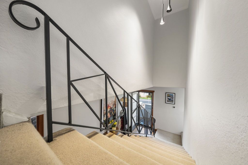 Indoor stairwell with beige carpet, black metal railing, and a bright hallway at the bottom.