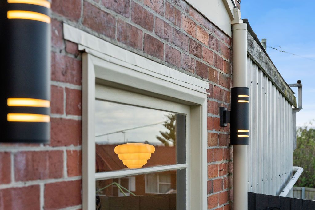 Brick house exterior with white-trimmed window and black wall lanterns near a fence
