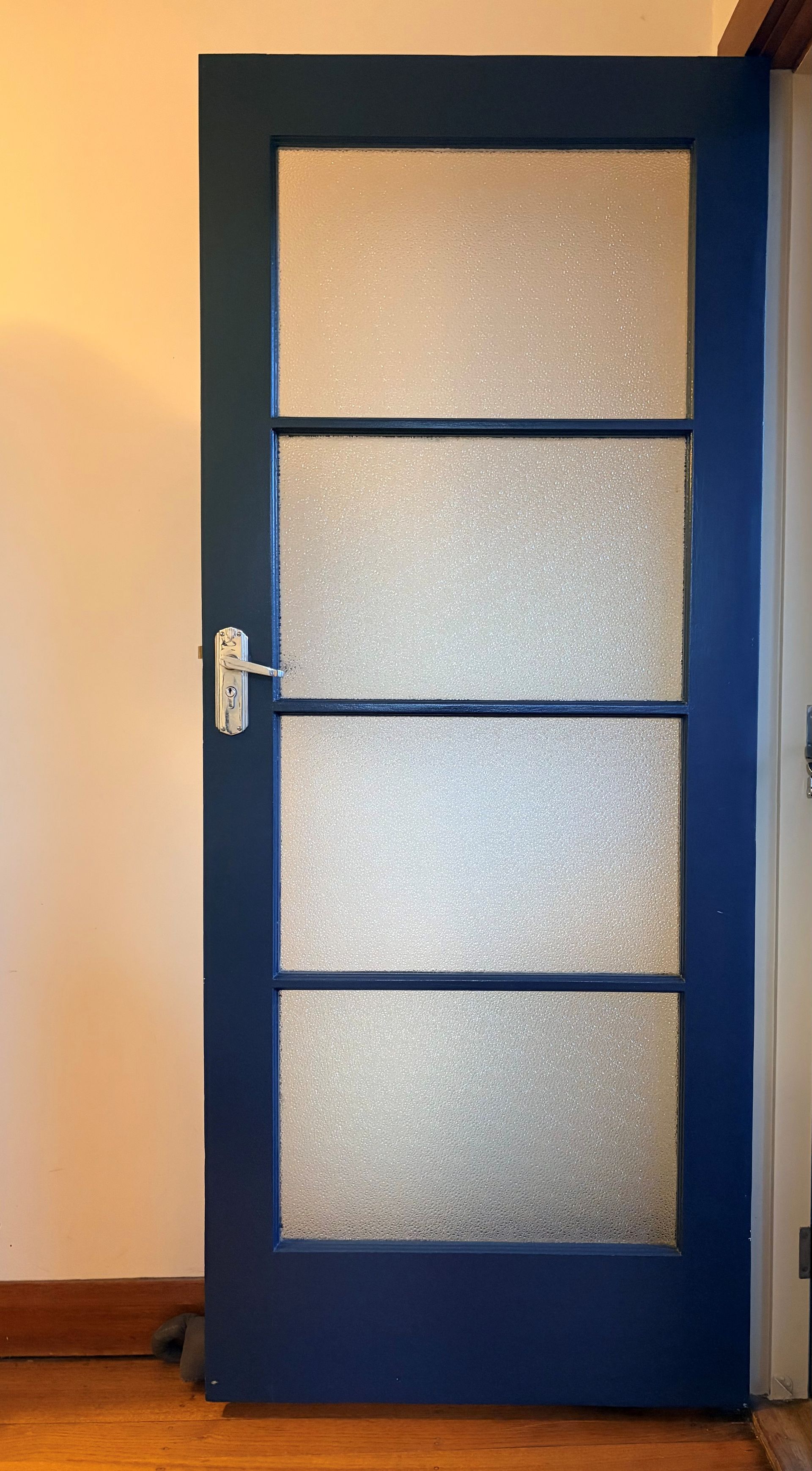 Blue door with frosted glass panels and a silver handle in an indoor hallway