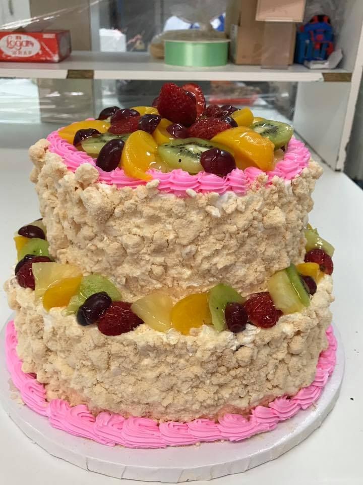 A two tiered cake with pink frosting and fruit on top.