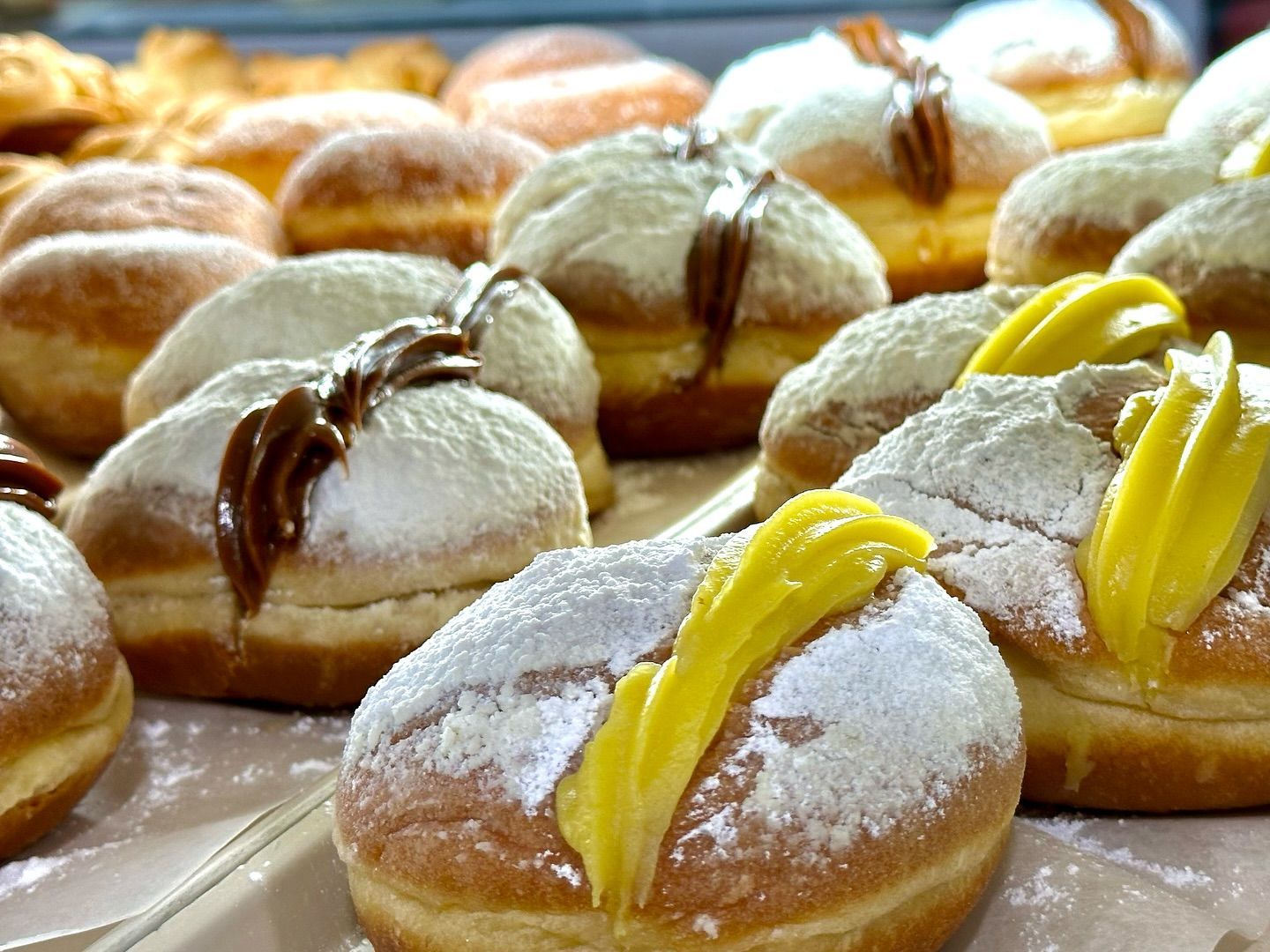 A bunch of donuts with powdered sugar and yellow frosting