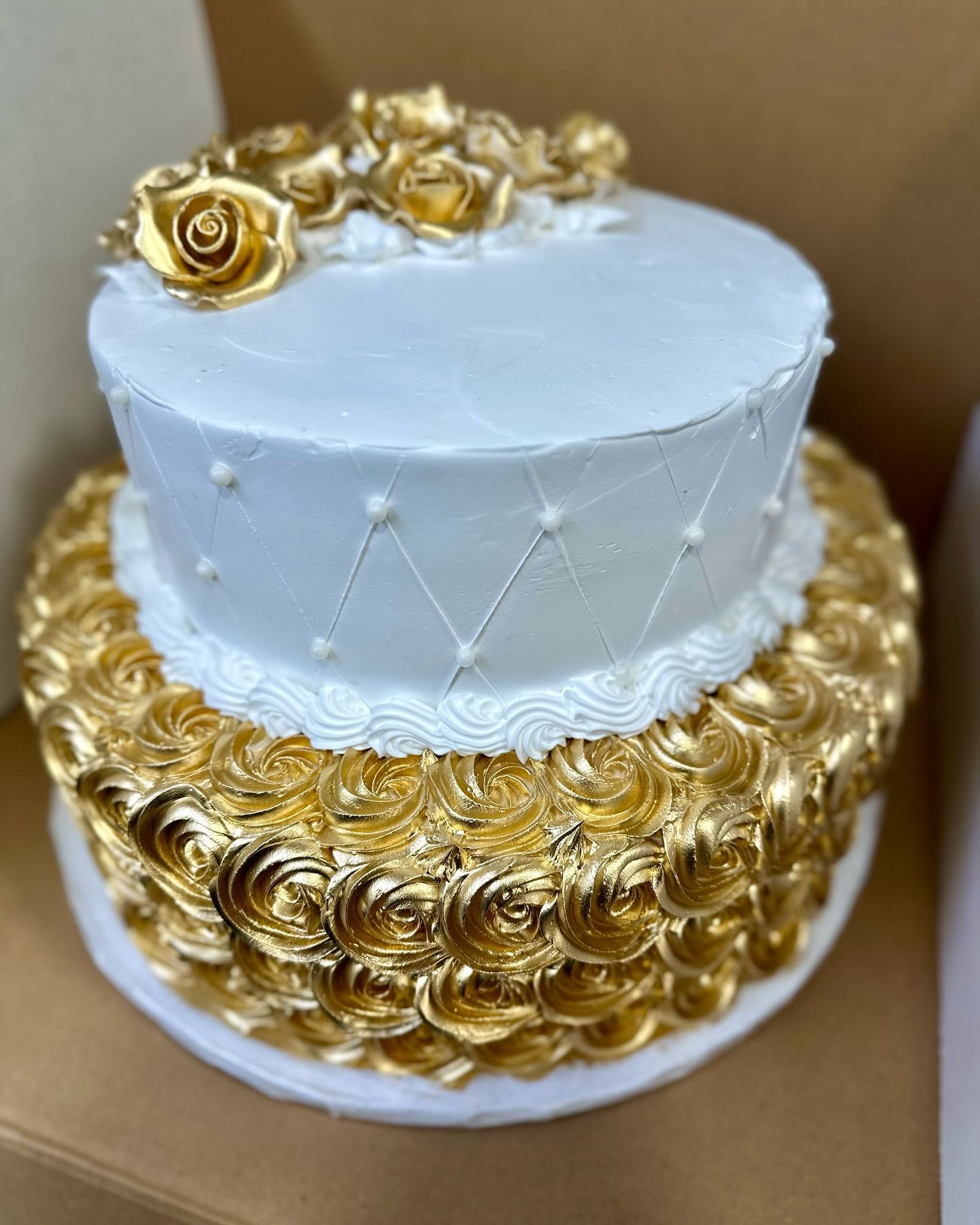 A white and gold cake with gold roses on top is in a box.