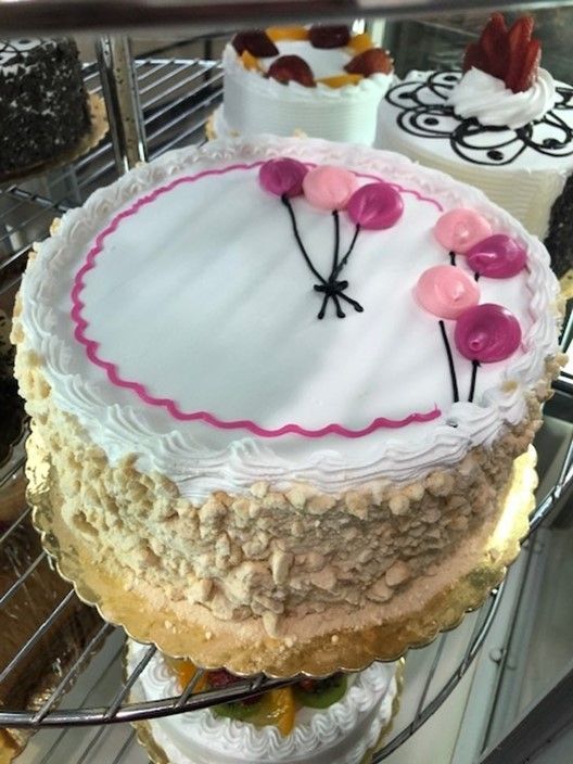 A white cake with pink flowers and balloons on it