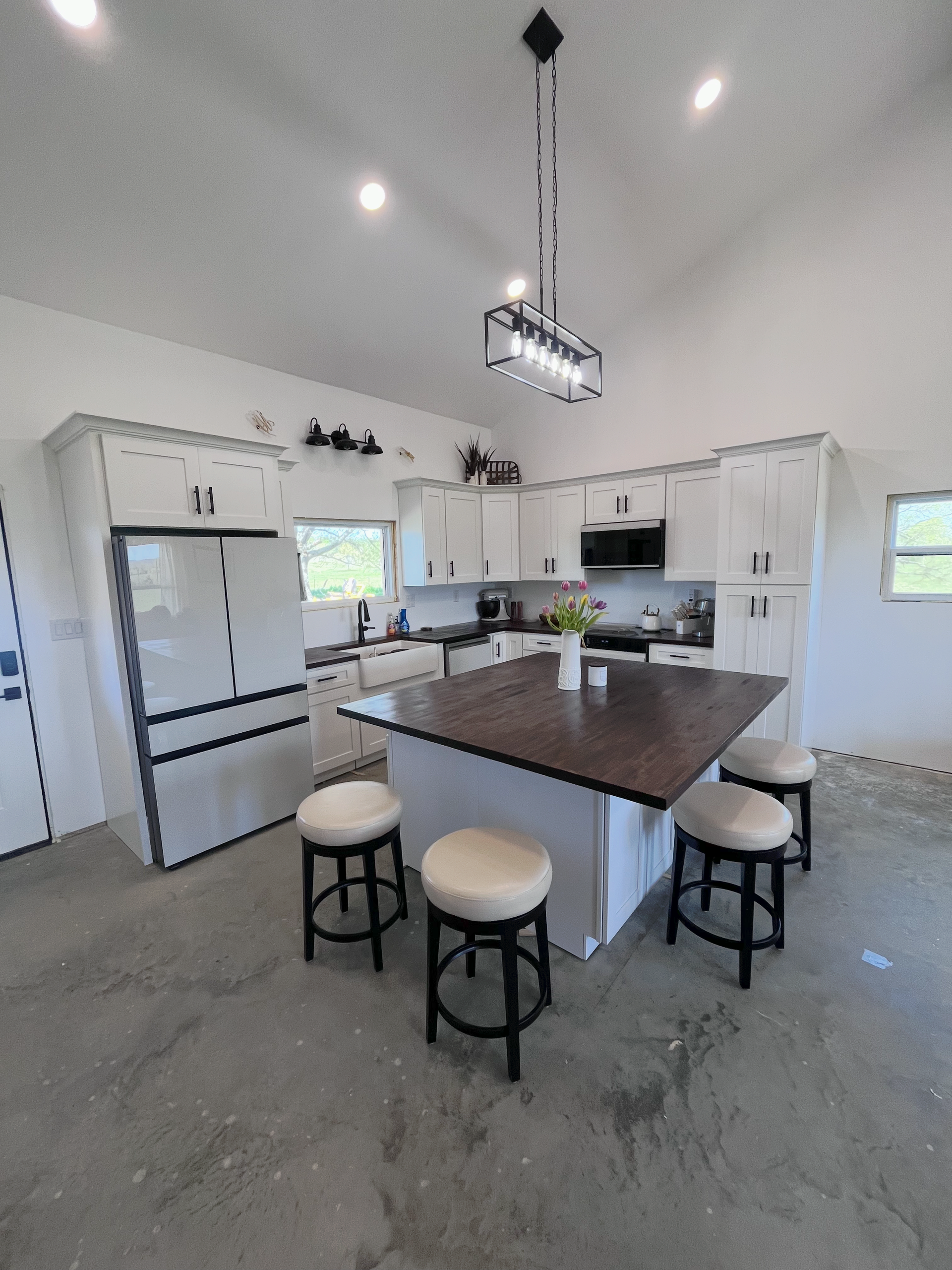 Bright modern kitchen with white cabinets, stainless fridge, island, and four stools