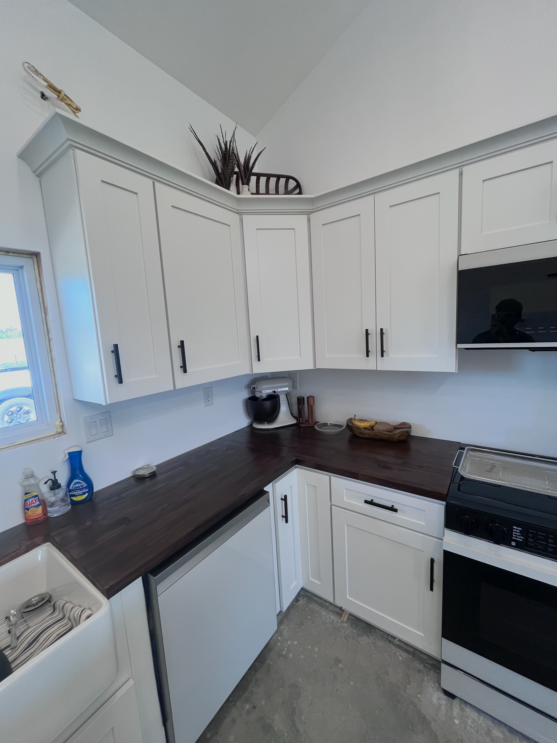 White kitchen with dark countertops, white cabinets, stove, dishwasher, and a window on the left.