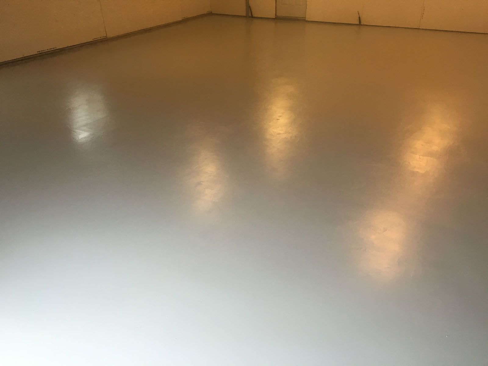 A smooth, light grey epoxy floor in an empty room with soft overhead lighting reflections.
