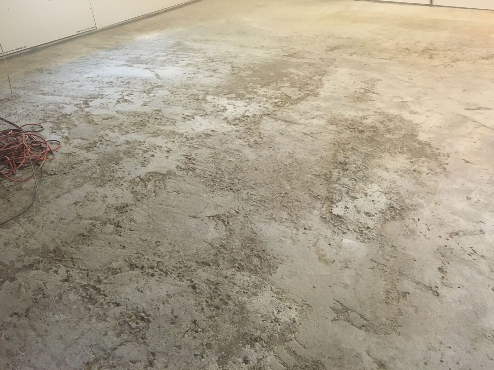 A rough, unfinished concrete floor in a room, featuring a textured, dusty, and uneven grey surface.