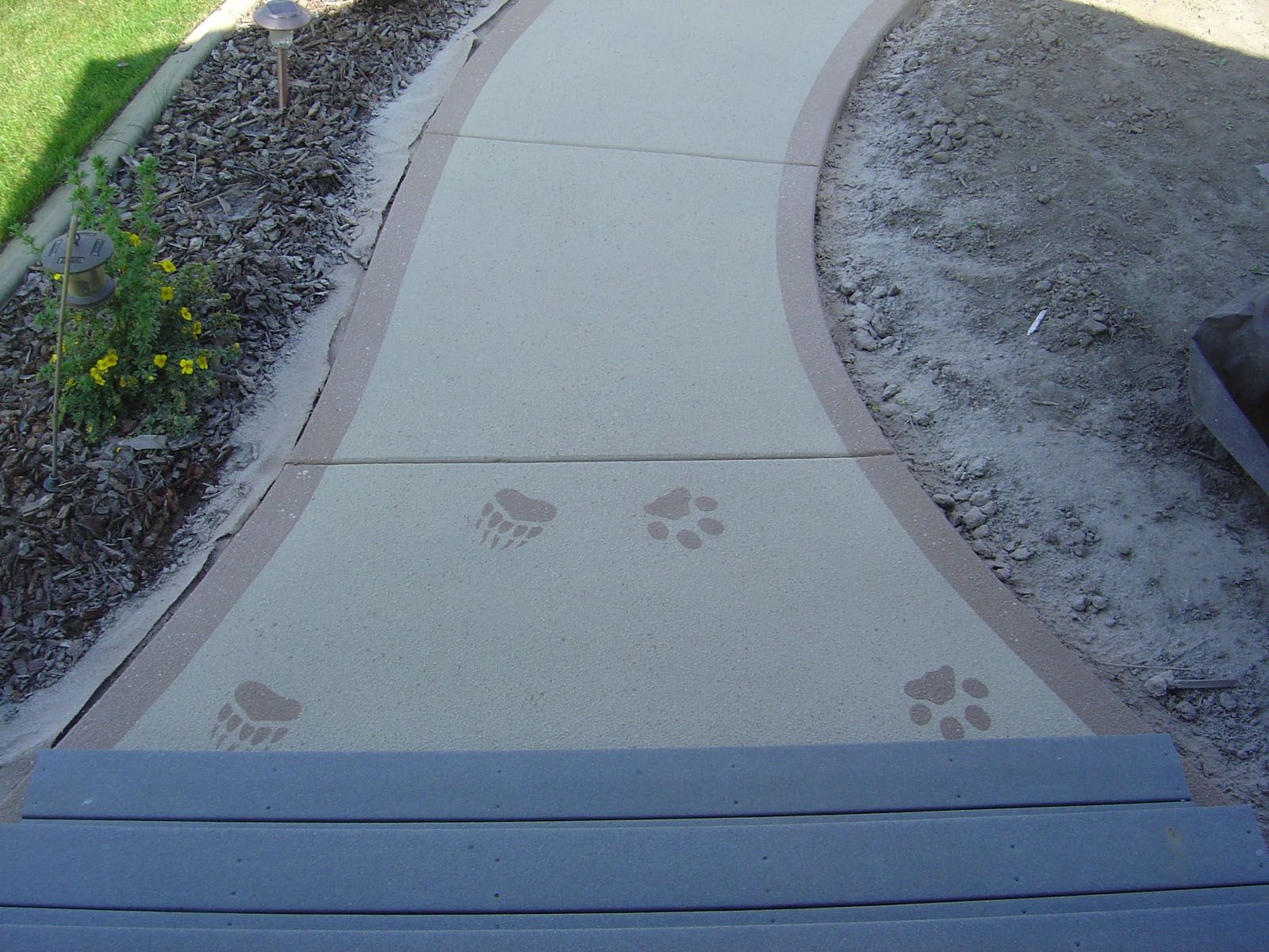 A curved concrete walkway featuring decorative bear and paw prints, leading away from a set of gray wooden steps.