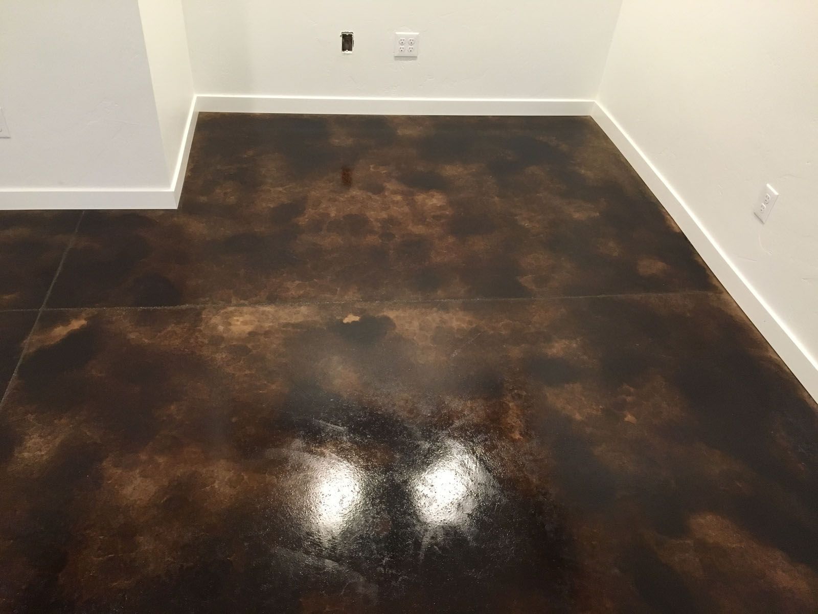 A room with a polished concrete floor featuring a mottled, dark brown and black stained finish against white walls.