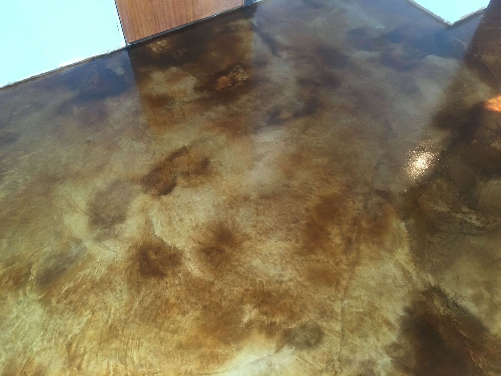 A close-up view of a polished concrete surface with a mottled brown and cream color pattern.