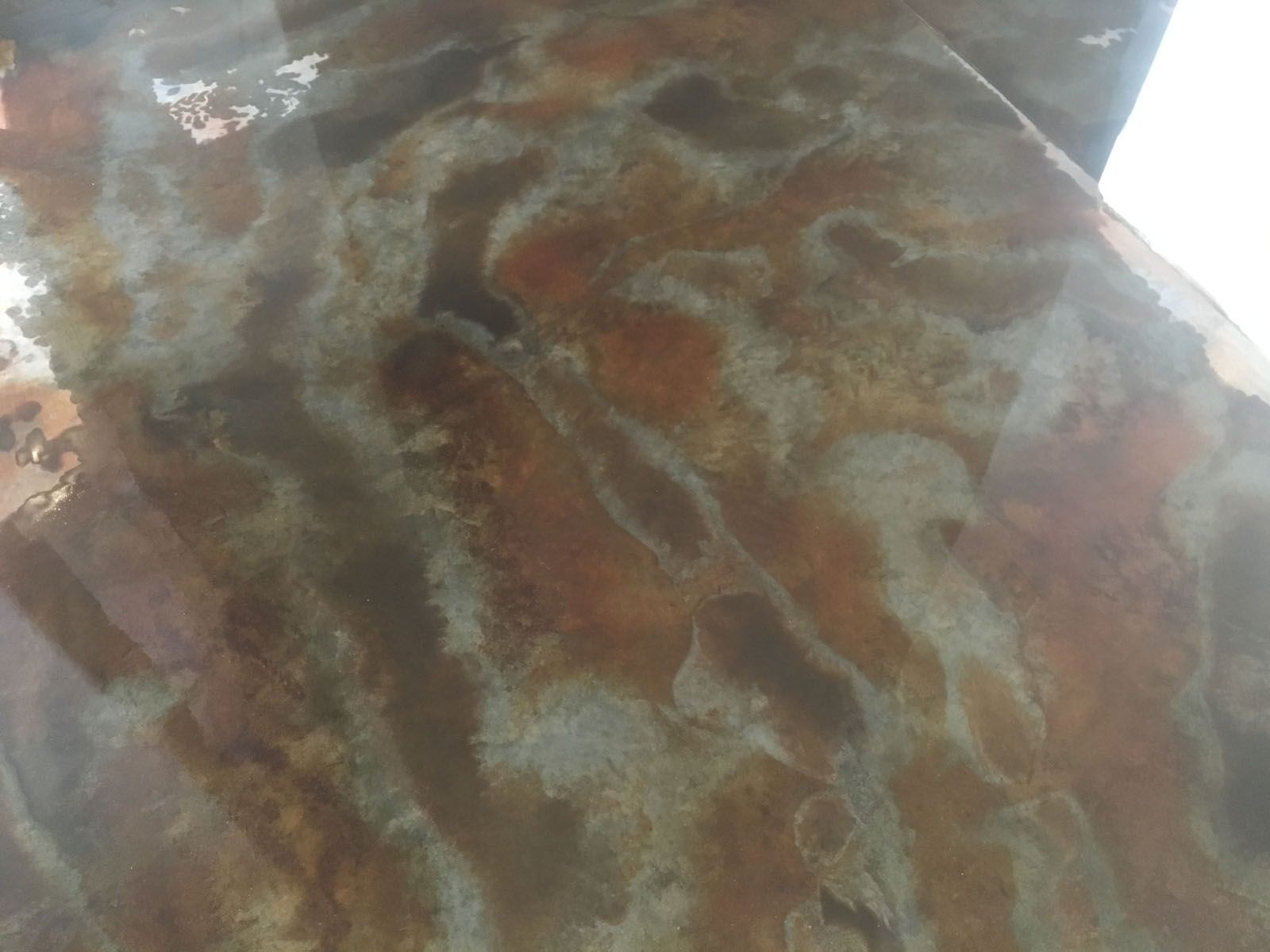 A top-down view of a glossy, mottled surface with swirling patterns of brown, tan, and grey, resembling polished stone.