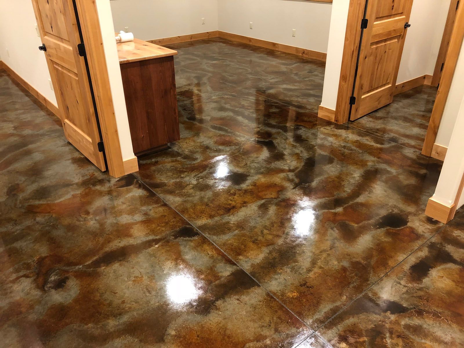 A polished concrete floor with a swirling, multi-toned brown and metallic finish in an interior hallway with wooden doors.