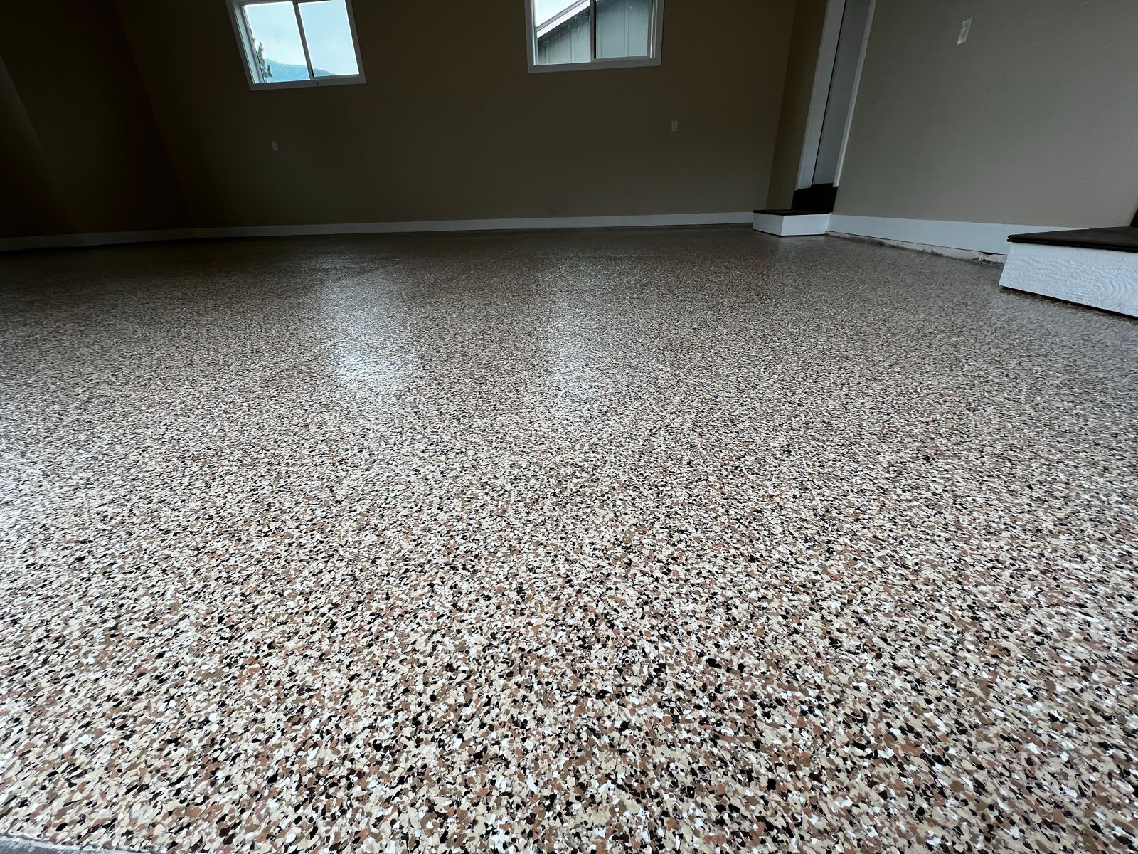 A view of a garage interior with a speckled, multi-colored epoxy floor and tan walls.
