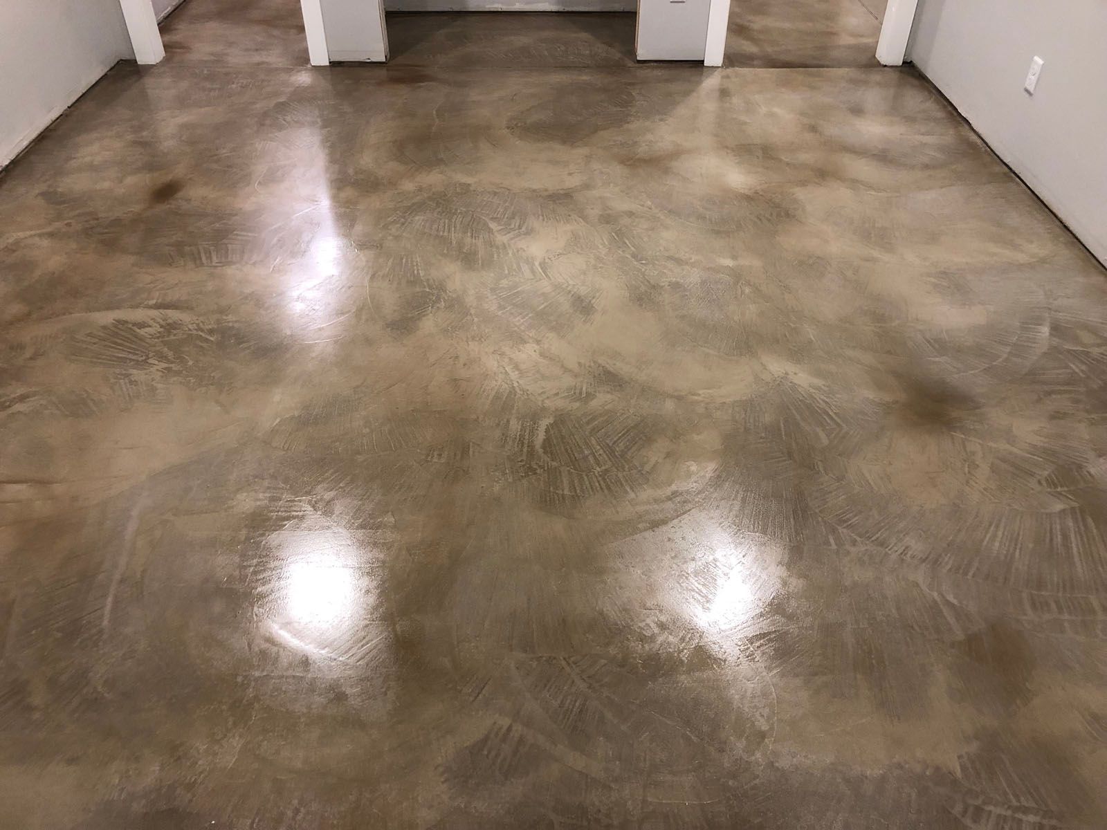 Polished concrete floor with a marbled, brownish-gray finish reflecting overhead light in an interior room.