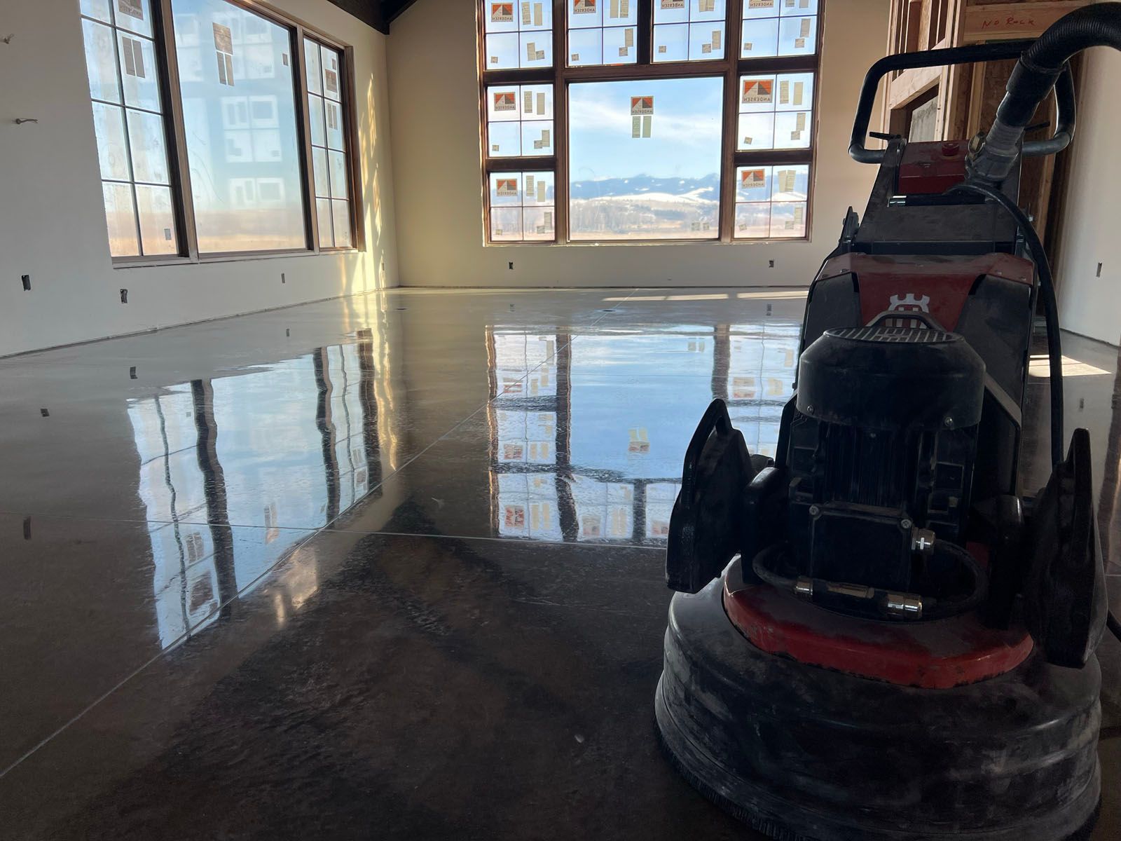 A commercial floor polishing machine sits on a newly finished, highly reflective concrete floor in a room with large windows.