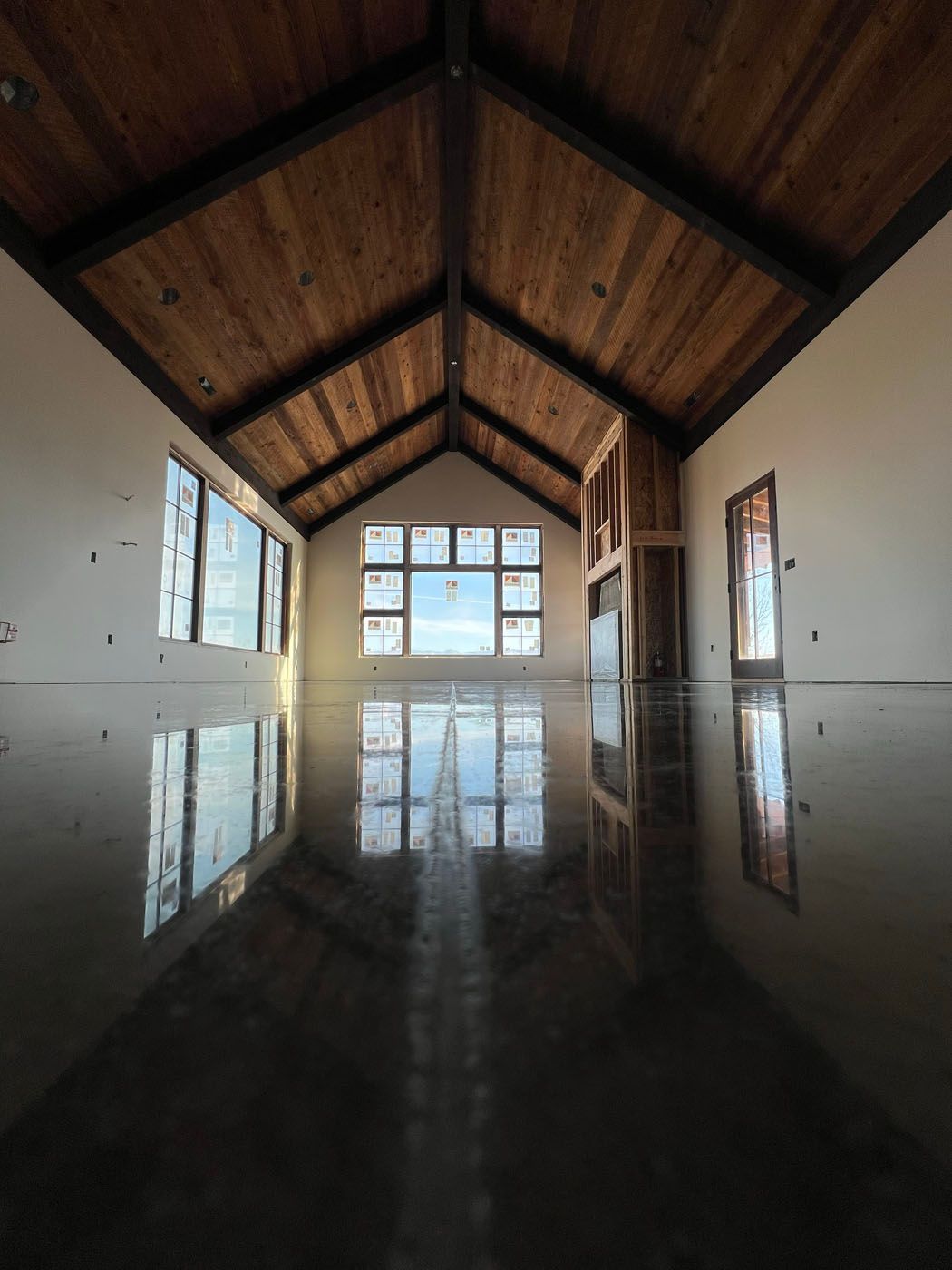 A spacious room under construction featuring a vaulted wood-paneled ceiling, large windows, and a highly polished floor.