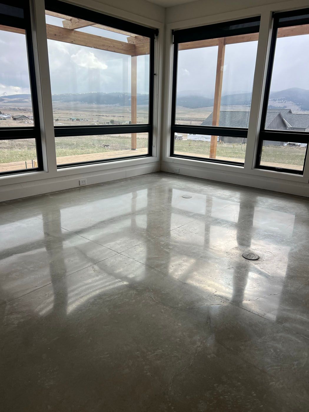 A sunlit room with polished concrete floors, large windows, and a scenic view of rolling hills and houses.
