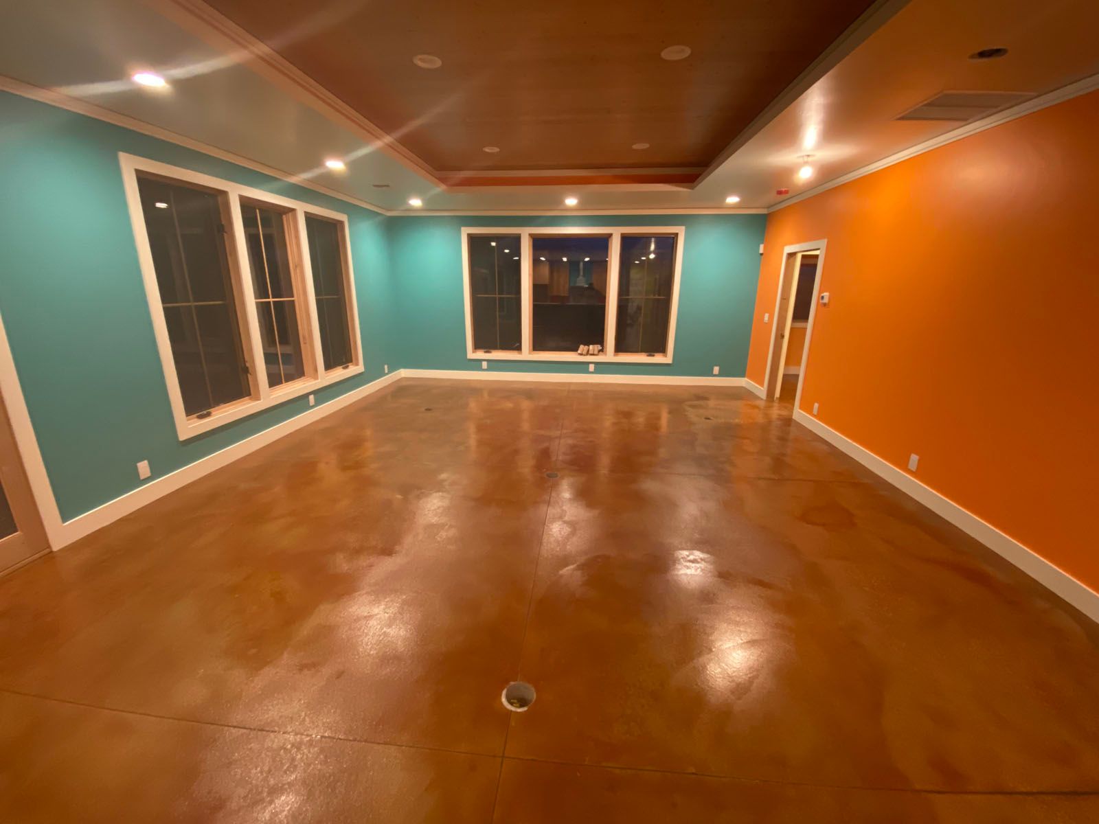Empty room with turquoise and orange walls, stained concrete floors, and a wood-paneled tray ceiling with recessed lights.
