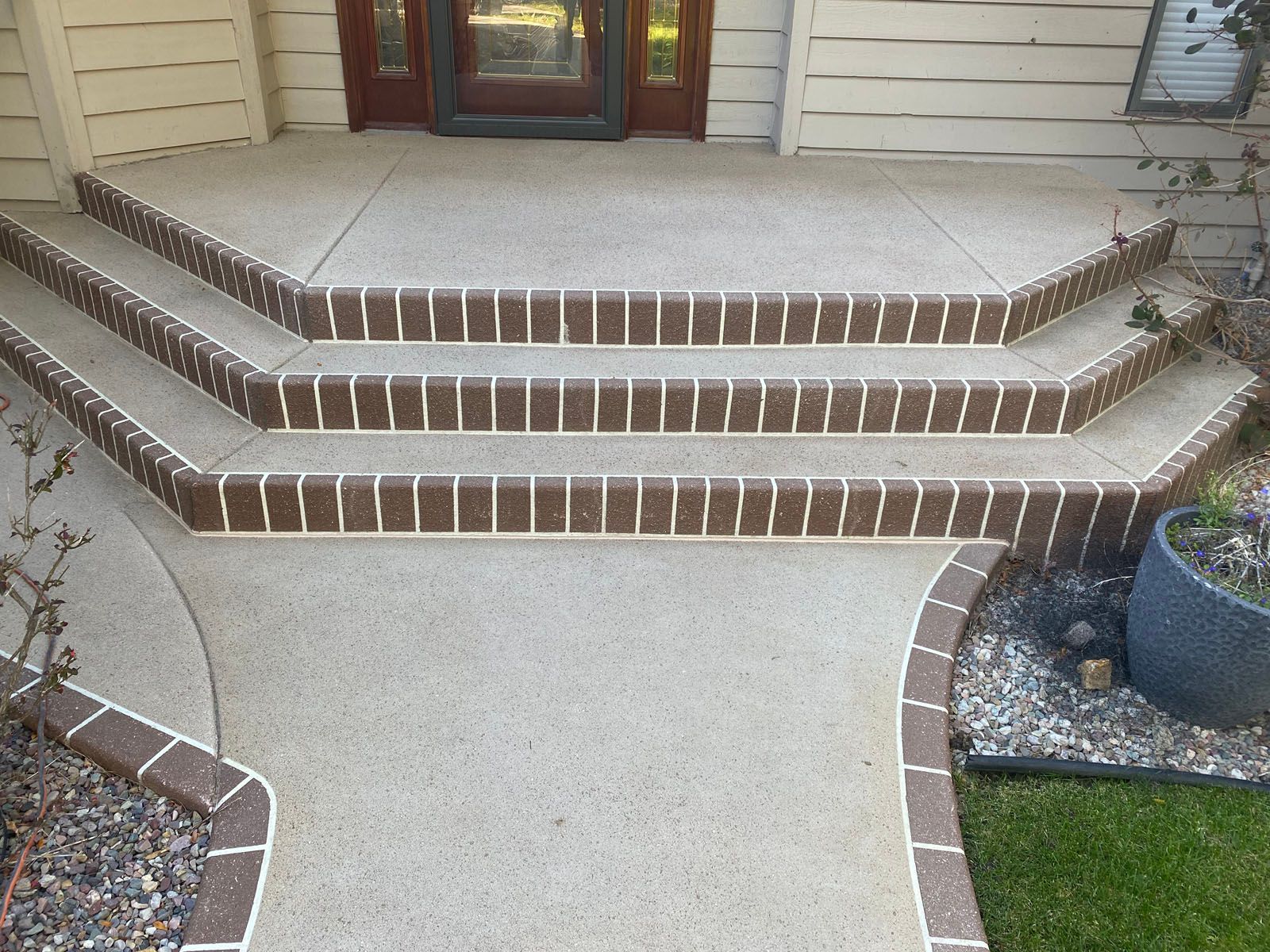 A porch with three concrete steps edged in brown brick, leading to a front door with wood siding.