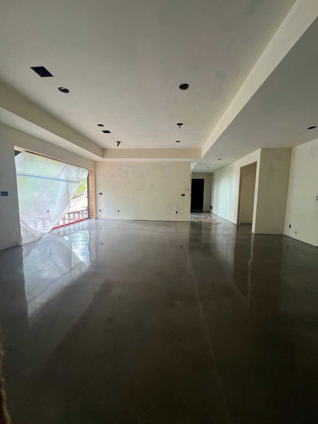 An expansive, unfinished room with a polished concrete floor, white walls, and a ceiling with recessed lighting.
