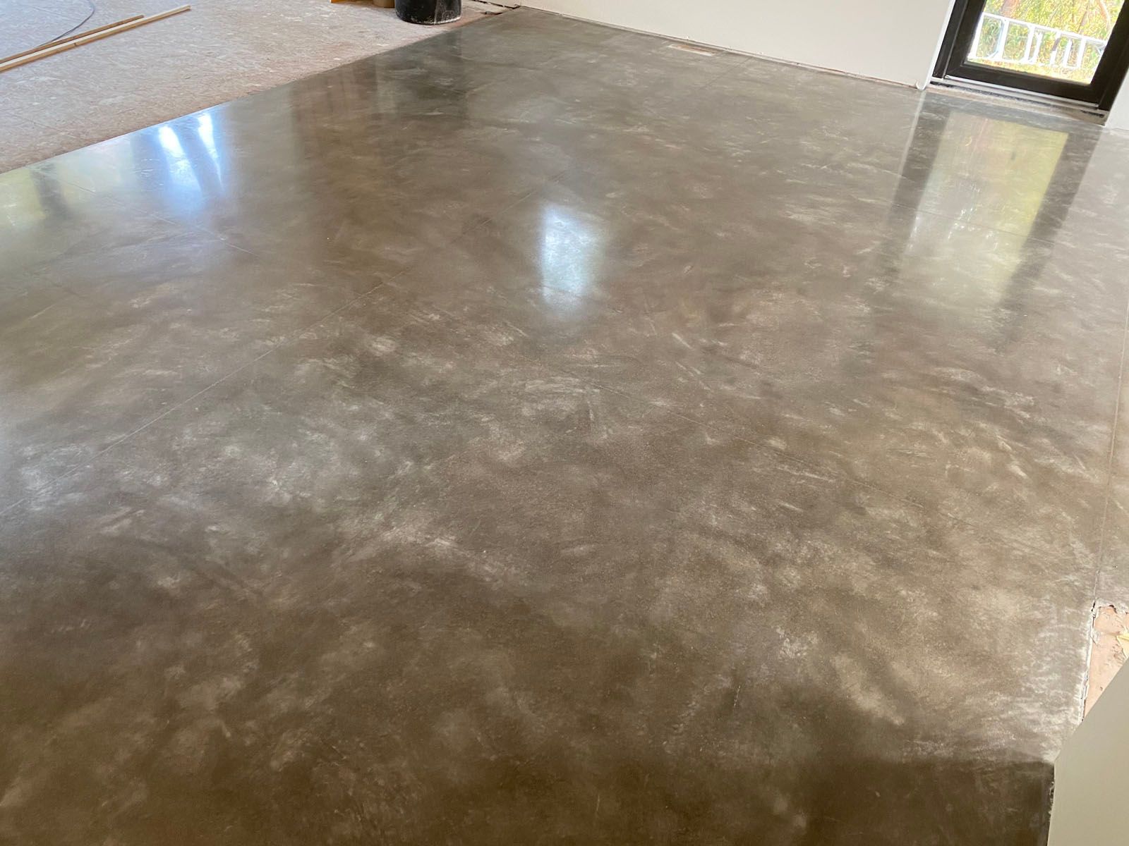 A polished, smooth concrete floor with subtle gray and brown mottled textures and light reflections.