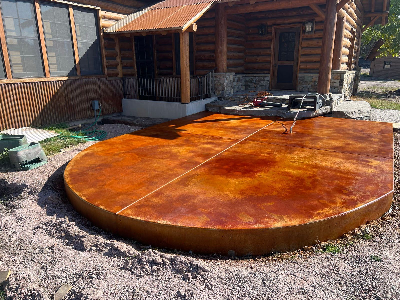 A semi-circular, stained orange concrete patio sits in front of a rustic log cabin home.