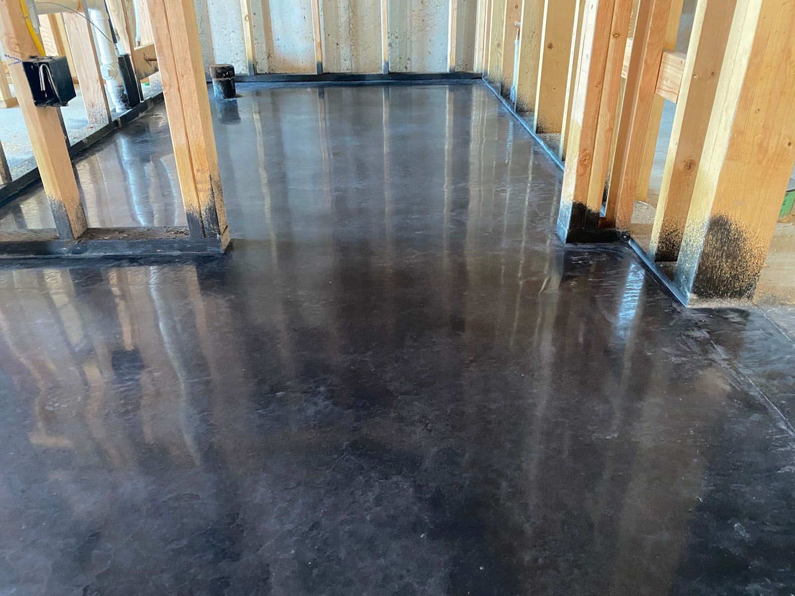 Polished dark gray concrete flooring in an unfinished room with exposed wooden wall studs.