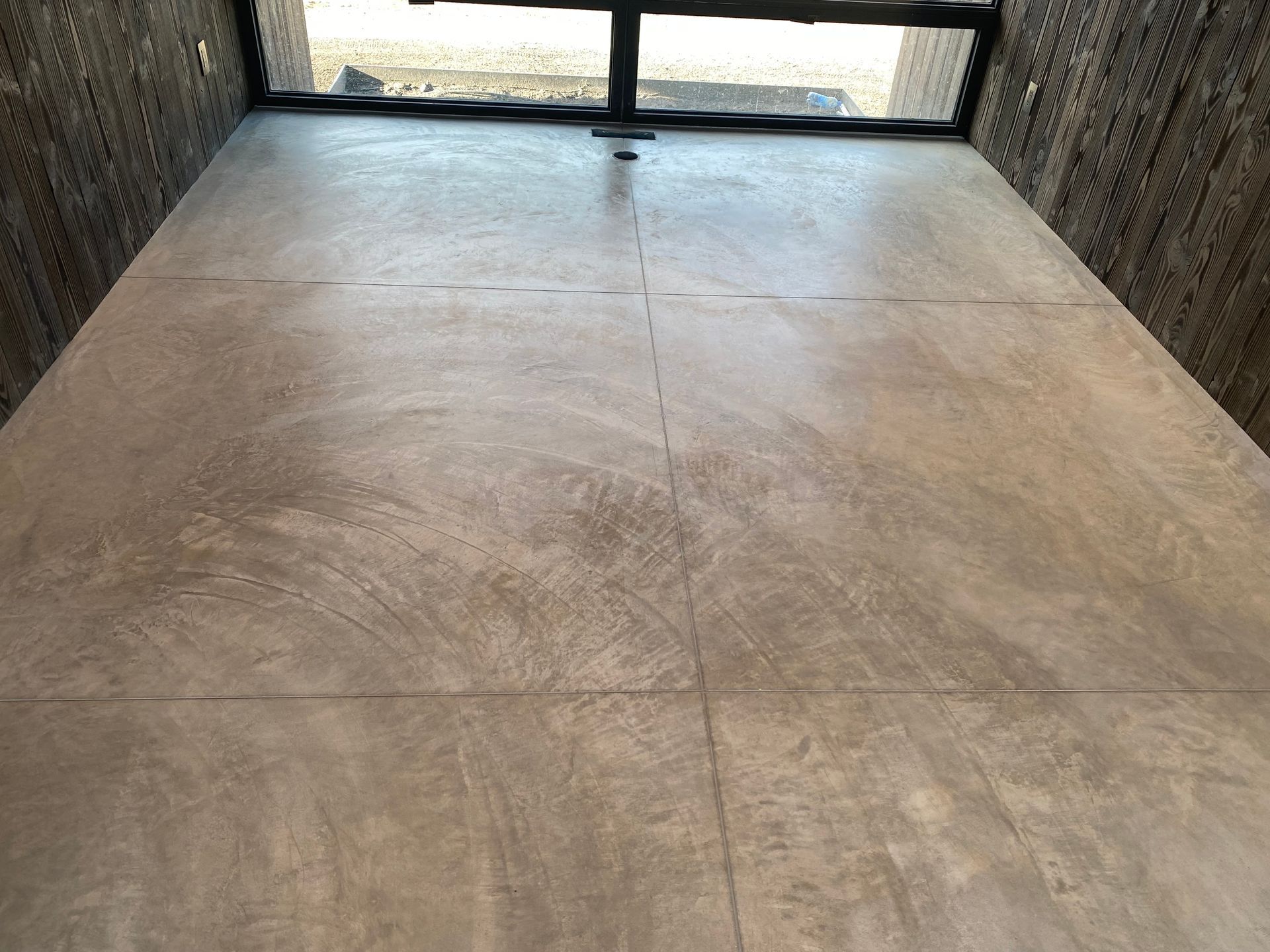 A room with a polished, light-brown concrete floor showing subtle circular trowel marks and visible control joint lines.