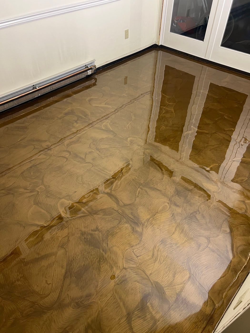 A high-gloss, bronze-toned epoxy floor with a swirling, marble-like pattern in a room with white walls and a radiator.