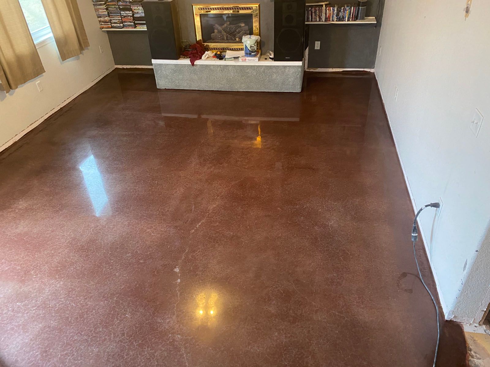 Polished brown concrete floor in a room with a fireplace, shelves, and beige curtains.