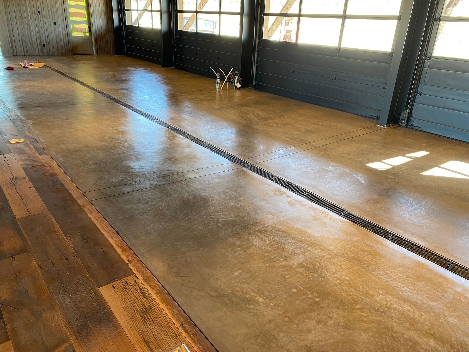 A polished concrete floor with a long metal drainage grate running through the center, next to dark wooden planks.