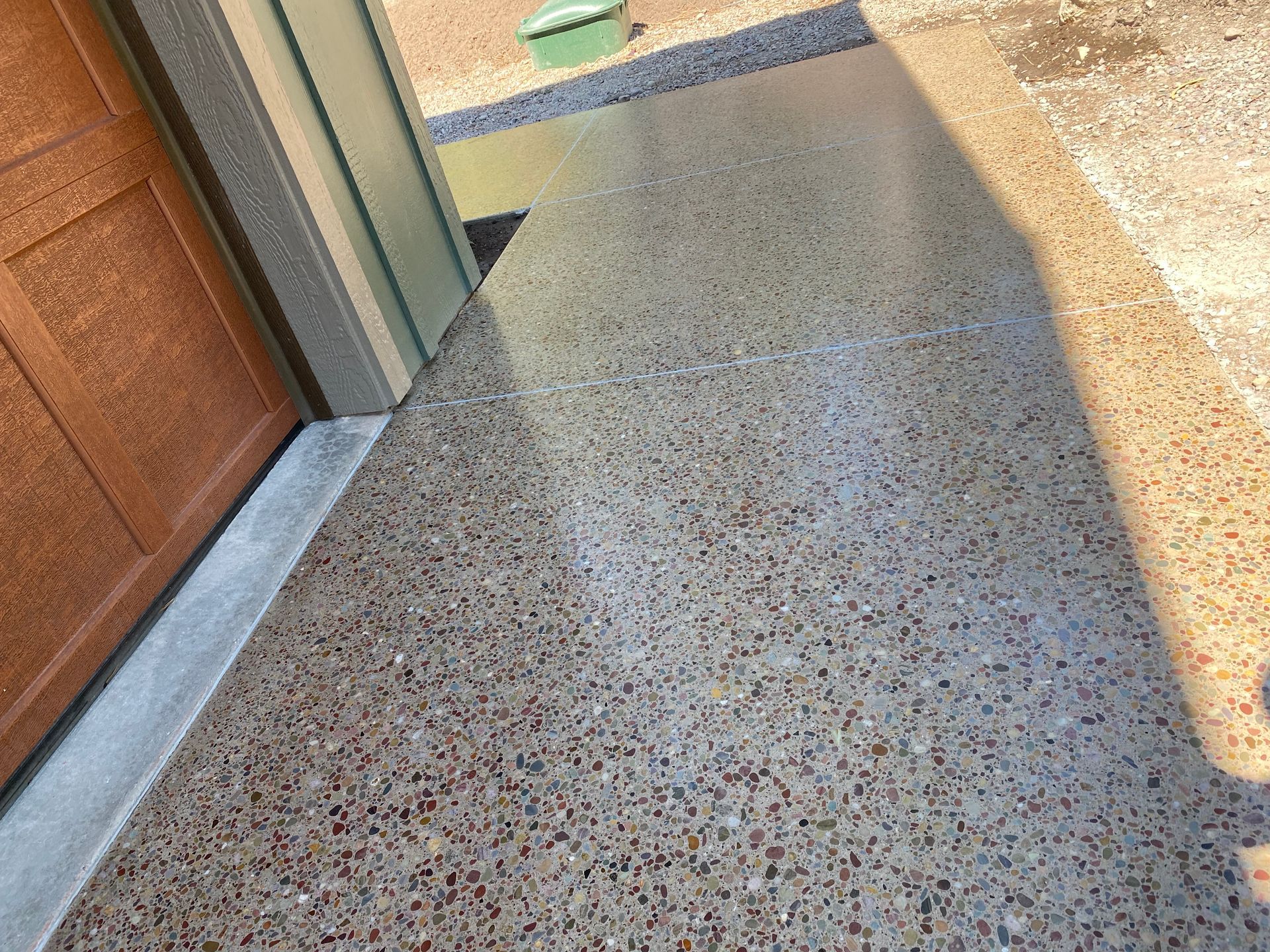 A close-up view of polished, speckled concrete flooring extending from a doorway towards an outdoor gravel area.